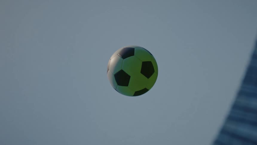 Soccer ball flies into the air above the sports field in a stadium during the daytime