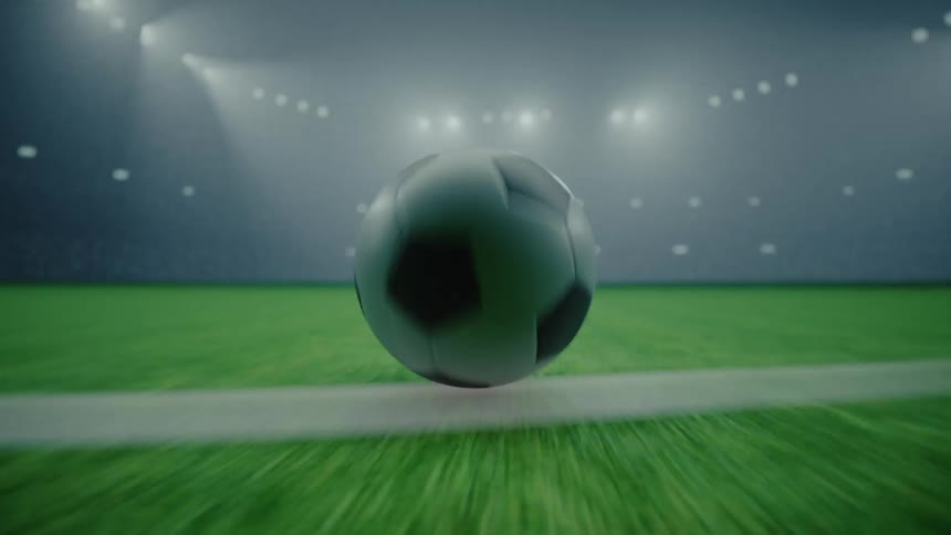 Soccer ball rolls across a brightly lit stadium soccer field at night