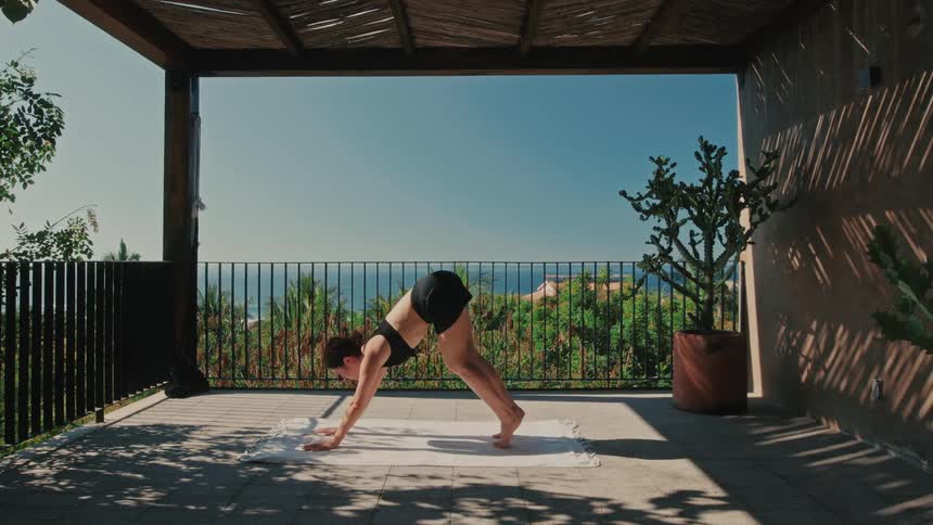 Woman bending down and stretching on a mat doing yoga exercises on her patio