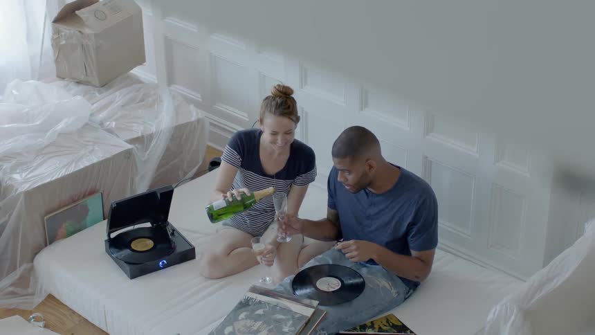 A couple are sitting on a mattress drinking champagne and listening to records