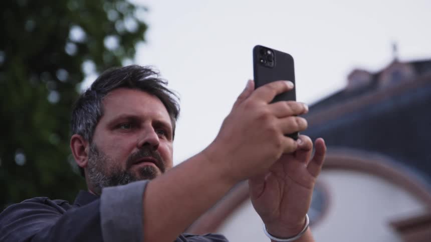 Man holding a smartphone to capture an image in an outdoor urban setting