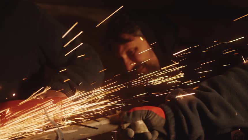 Man working with a metal cutting tool producing sparks in a dark environment