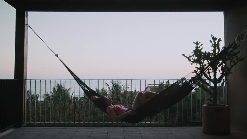 Woman sleeping in a hammock on a terrace overlooking the sea