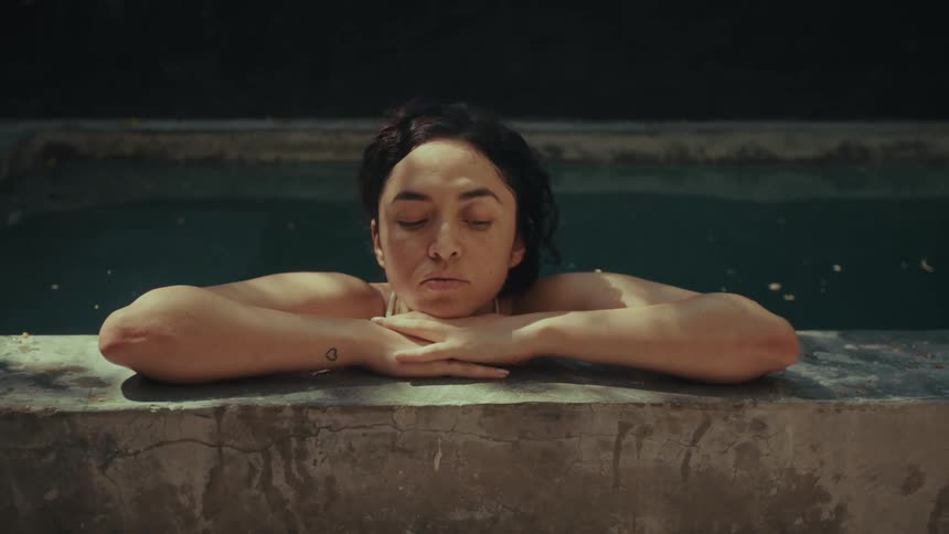 A woman soaks in a rustic stone pool gazing up for a moment before closing her eyes and resting peacefully on the sunwarmed edge finding a moment of serene tranquility