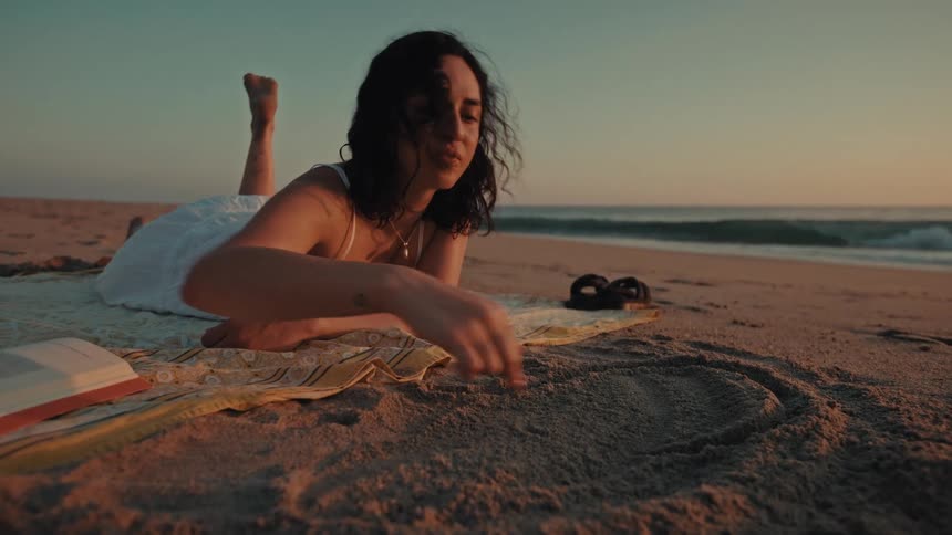 Woman drawing a heart in the sand on the beach at sunset