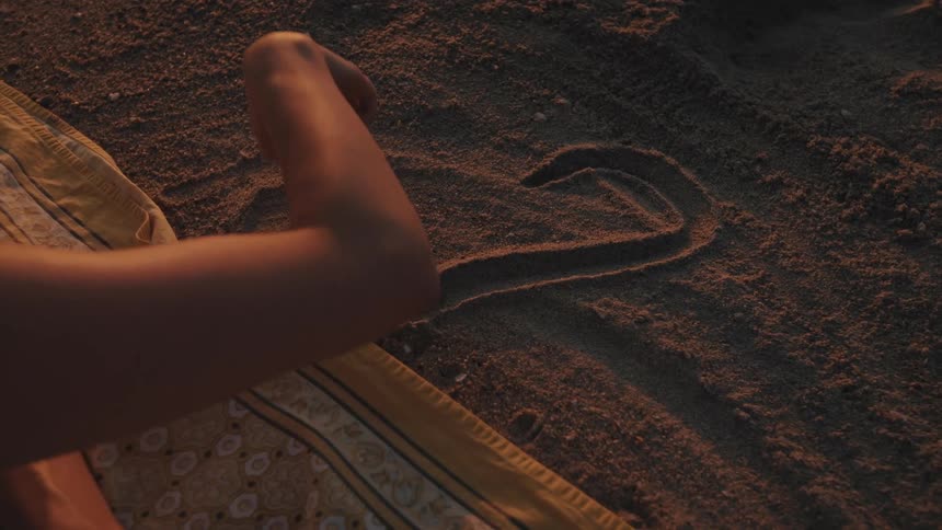 Woman draws a heart in the sand then wipes it away