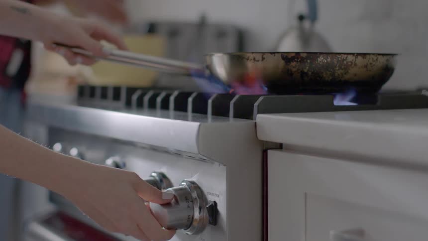 Woman lights burner under a pan in the kitchen