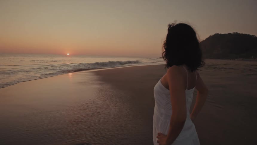 Woman standing at the shoreline watching the sunset over the ocean