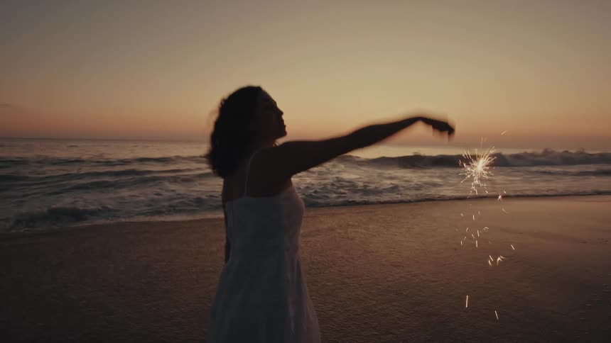 A woman playing with a sparkler on a beach