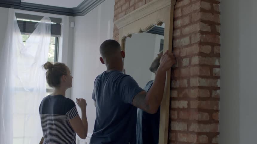 Man and woman putting a large mirror on the wall in a house