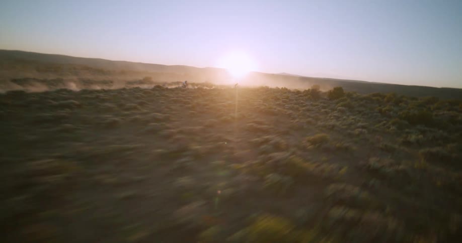 Two people ride a motorcycle through a dusty desert bathed in golden hour sunlight