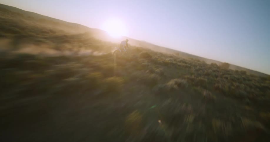 Cyclist on a motorcycle rides across rural land as the sun shines in the distance