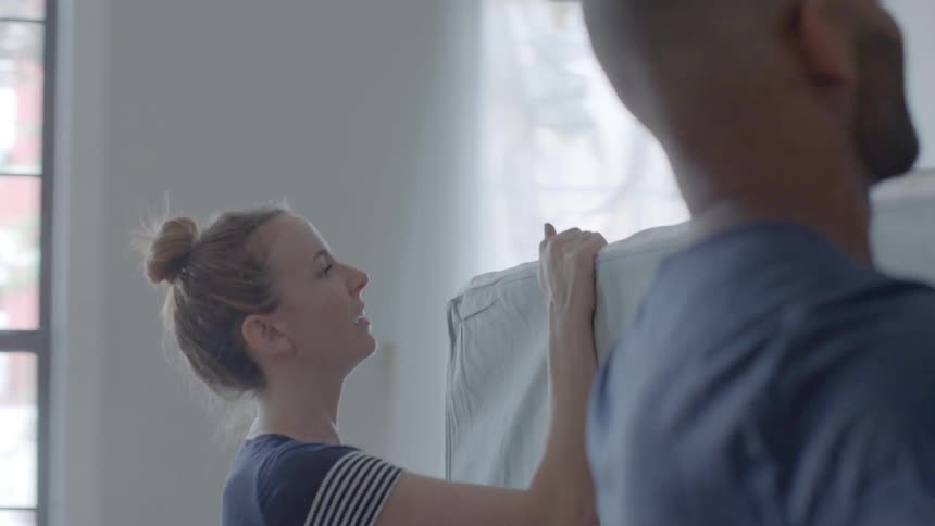 A man and woman carry a mattress into a home
