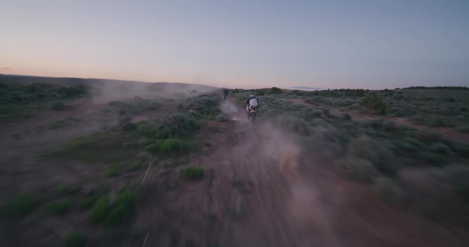 People race dirt bikes across a track in a field while the sun sits just beneath the horizon
