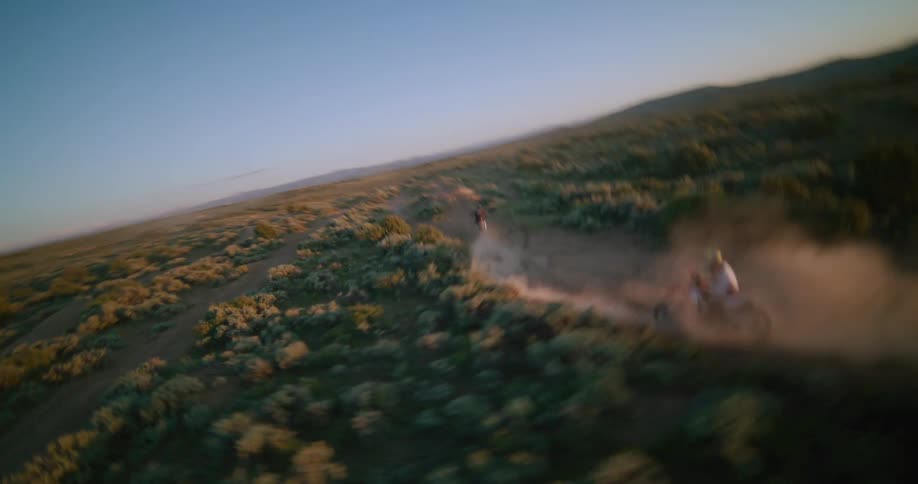 Two people on motorcycles ride across the rural terrain leaping off hills