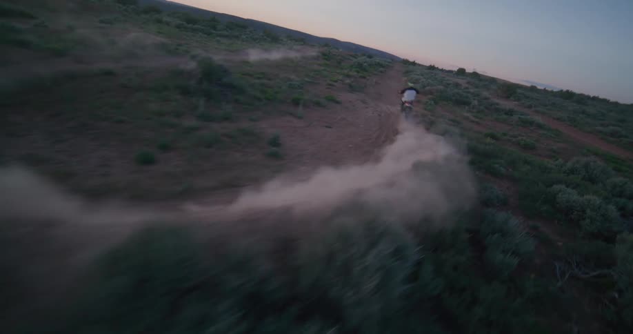 Motocross riders performing stunts on a trail at dusk