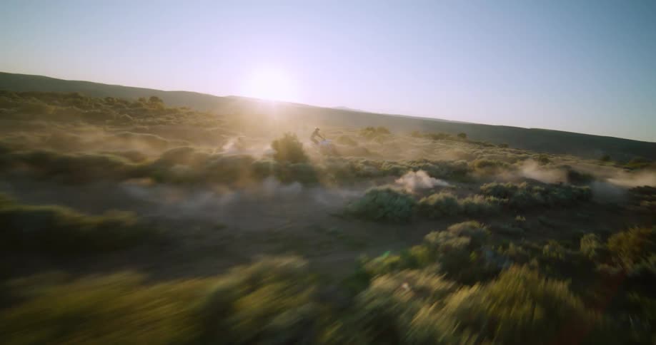 Biker riding a motorcycle on a dust road surrounded by vegetation outdoors during dusk or dawn
