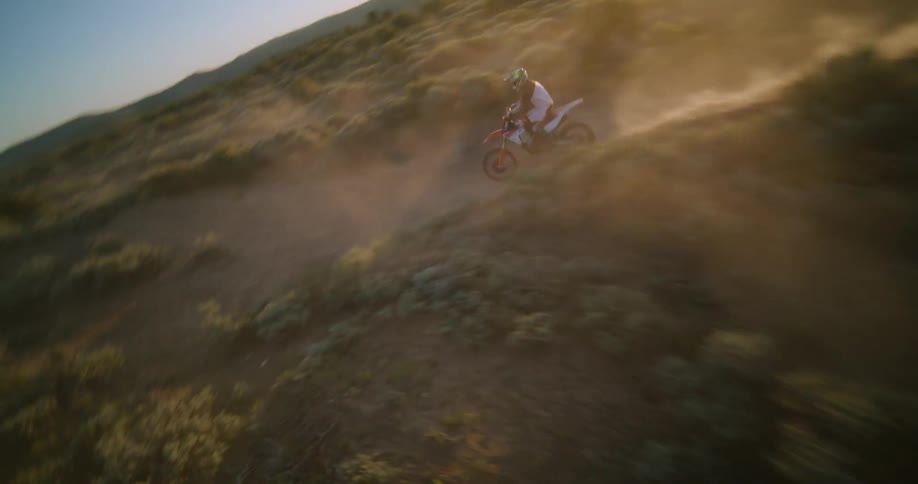 Biker riding a motorcycle on a dust road surrounded by trees and vegetation outdoors during dusk or dawn