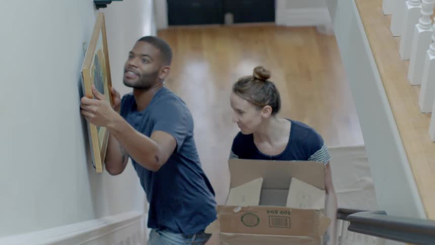 A man places a portrait on the wall as a woman climbs the steps