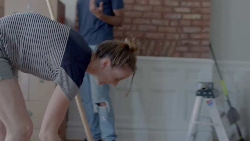 A man and woman clean a living room while moving in