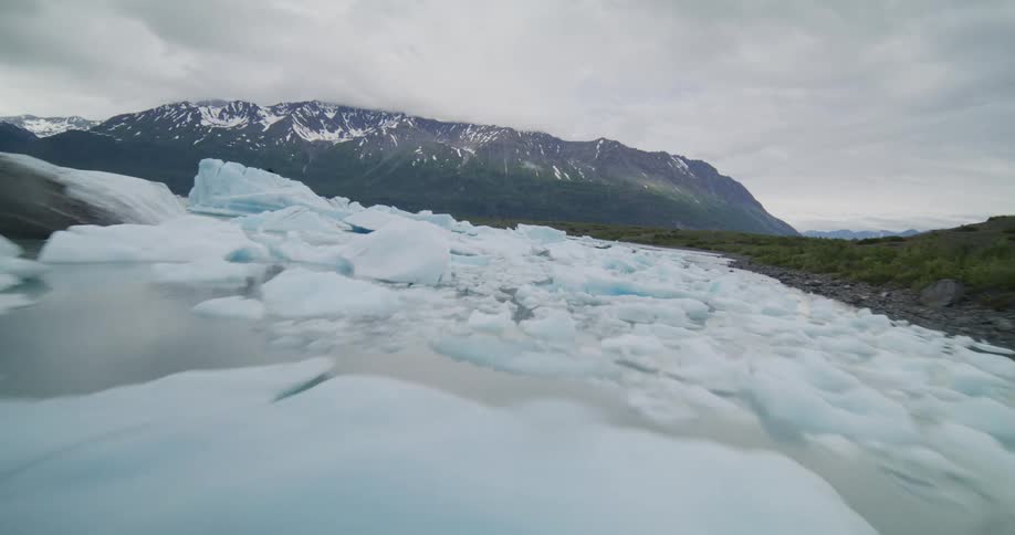Mountains and hills surround a body of water filled with floating pieces of ice on an overcast winter day