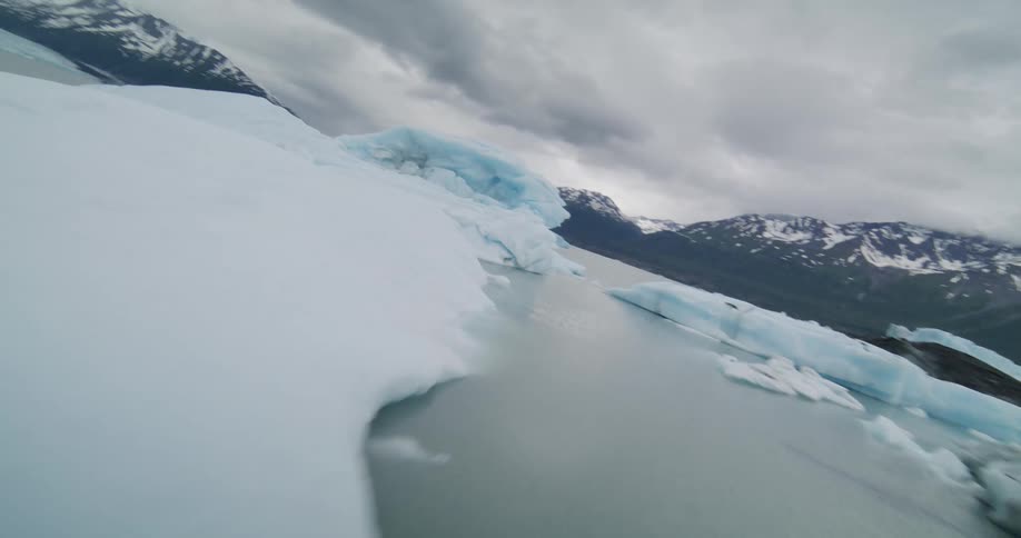 Ice blocks float on a glacial lake surrounded by snowcovered mountains under a cloudy sky