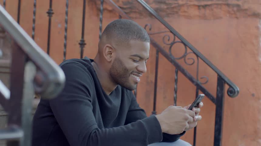 A man is smiling using his phone on the steps
