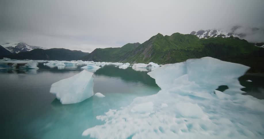 Aerial view of a calm bay with icebergs surrounded by green mountains under cloudy sky