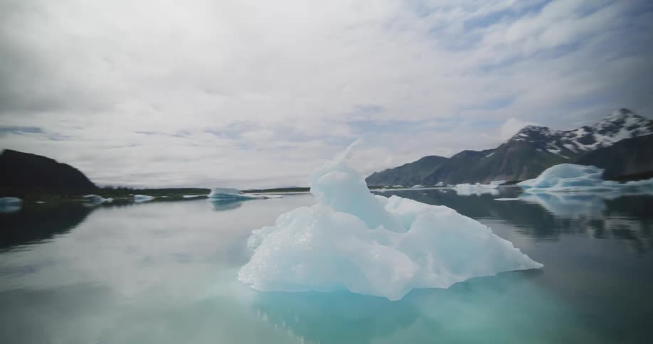 An iceberg floats on a calm lake at midday with a mountain rising in the background