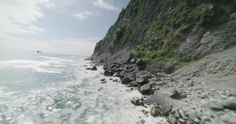 Waves splash into rocks at the foot of a mountain cliff along the coast