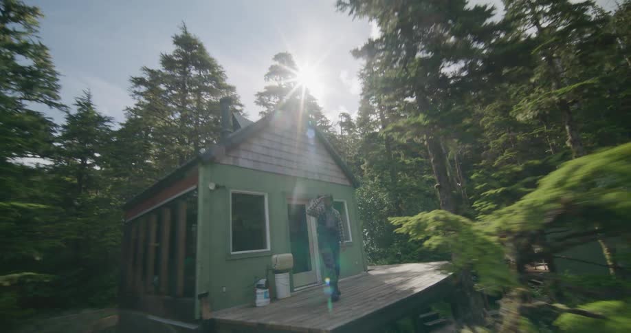 A drone zooms backward from a forest cabin through the trees to reveal a lakeside helicopter dock