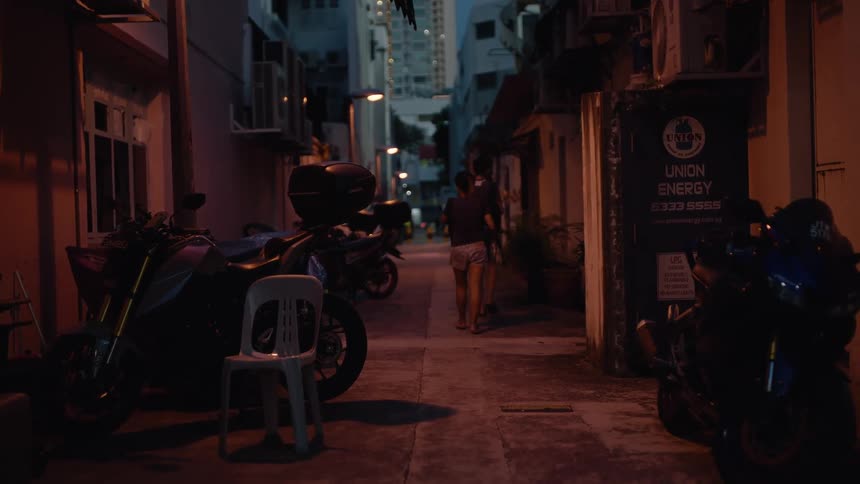 A man and a woman walk away down a dimly lit alleyway lined with motorcycles