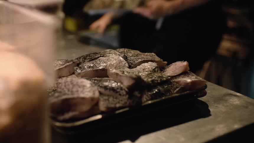 Seasoned raw fish fillets rest on a metal tray in a professional kitchen