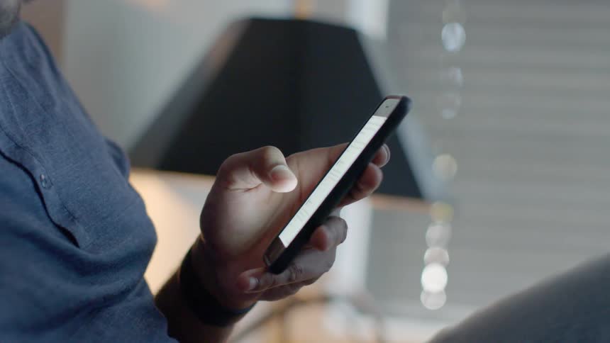 A man scrolls on a smartphone in bed