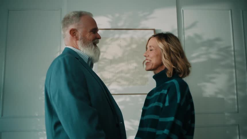 Man and woman smile and face each other while holding hands between them