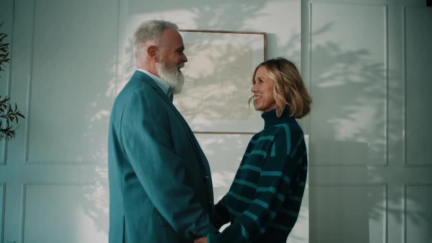 Couple facing each other holding hands in an indoor setting with natural light