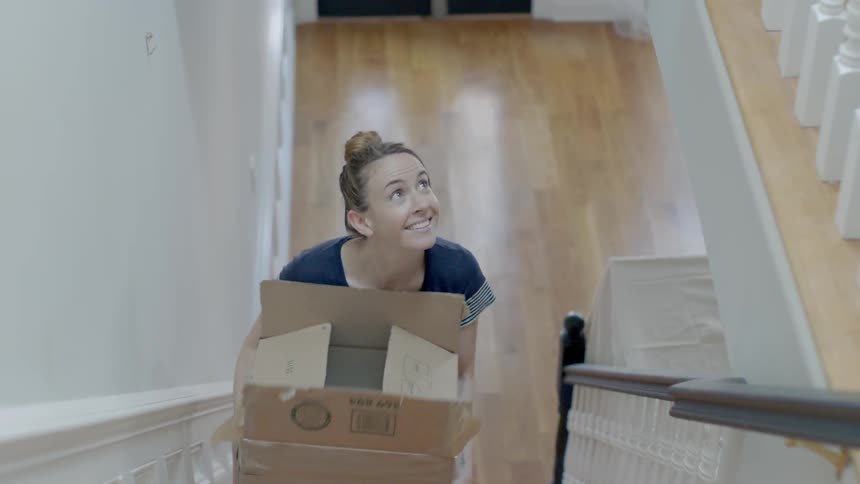 A woman in a blue shirt walks up the steps carrying a box