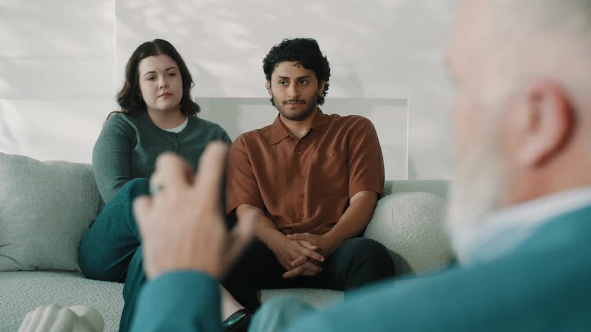 A man talking to a man and woman sitting on a couch