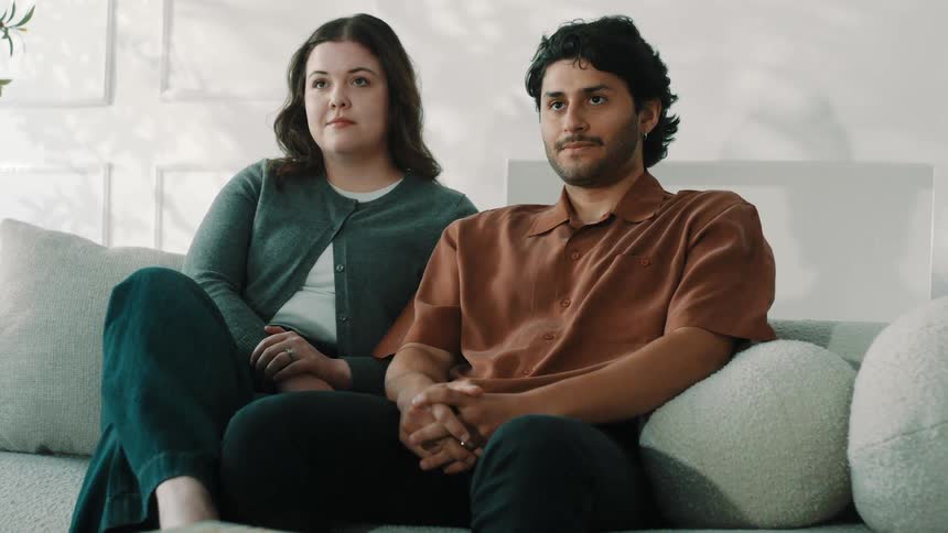 Couple seated on a sofa listening to a conversation in a naturally lit indoor setting