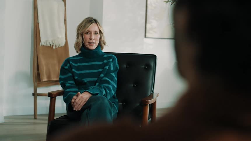 Two people sit calmly attentively engaging in a conversation in a softly lit indoor space