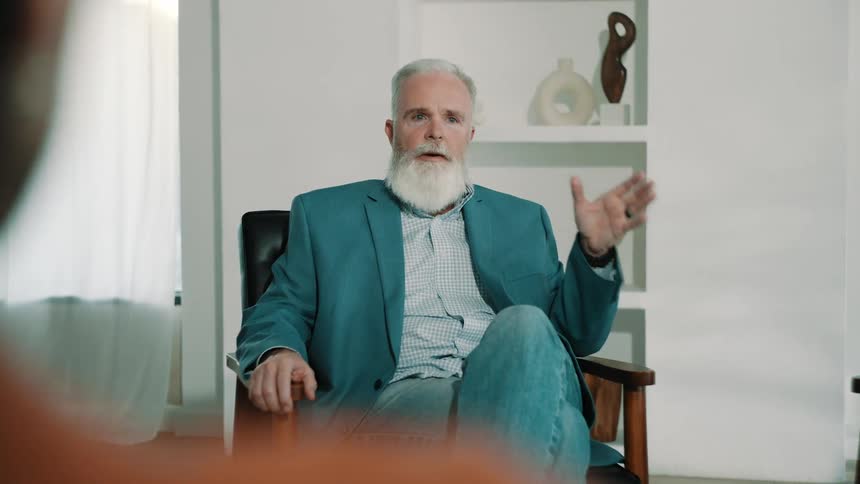 A person listens as an elderly man talks and moves his hand