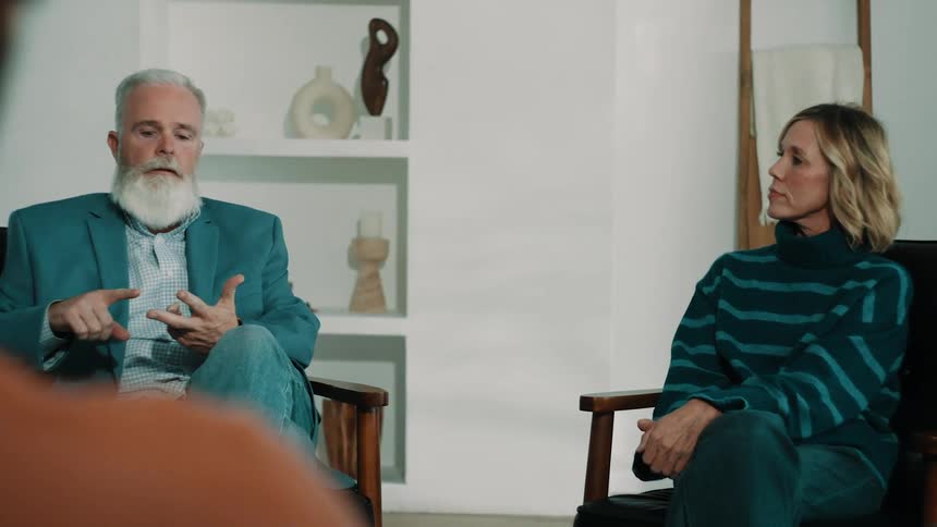 An elderly man is talking as two other people sit and listen