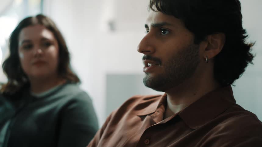 Man speaking during a conversation in an indoor setting with another person in the background