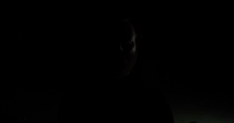 A man with a red beard and a nose ring appears against a completely dark background as the lighting quickly fades in and out