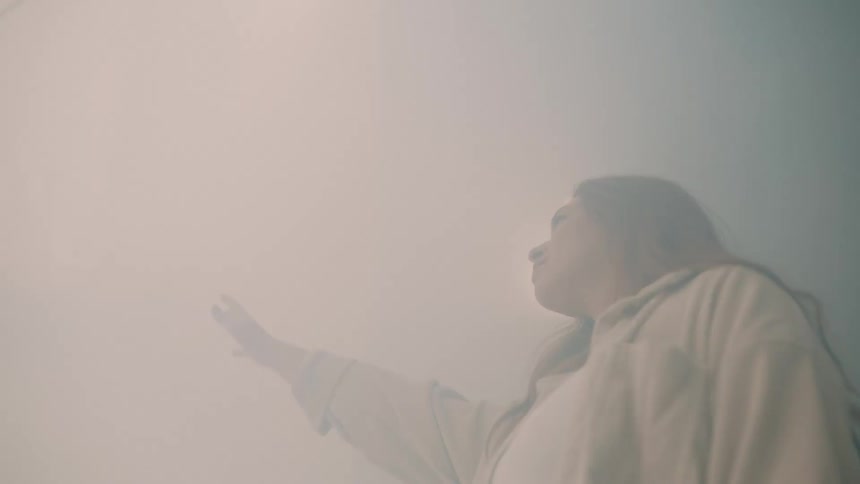 Woman reaches her right arm up through fog with lights shining through from behind