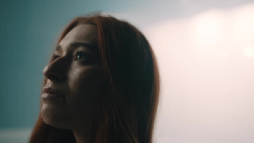 A woman with long hair interacts with a large white fabric sheet in a room filled with thick swirling mist the cinematic lighting shifts dramatically between warm hazy orange glows and moody cool blue tones as the camera captures her profile and movem