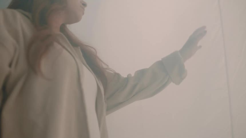 Woman reaching toward a white curtain in a softly lit environment