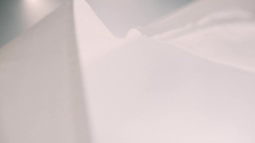 A close up low angle shot shows white thin fabric billowing and rippling like clouds against a bright background