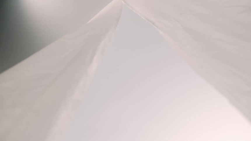 A white thin fabric or plastic sheet hangs from above and sways gently in the air the material is translucent and creates a bright airy atmosphere against a pale background