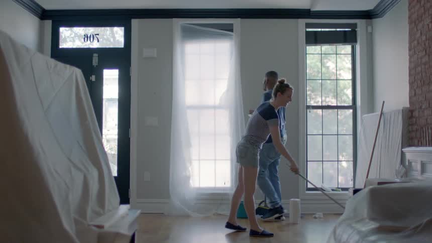 A man and woman clean the floor and windows in the front room